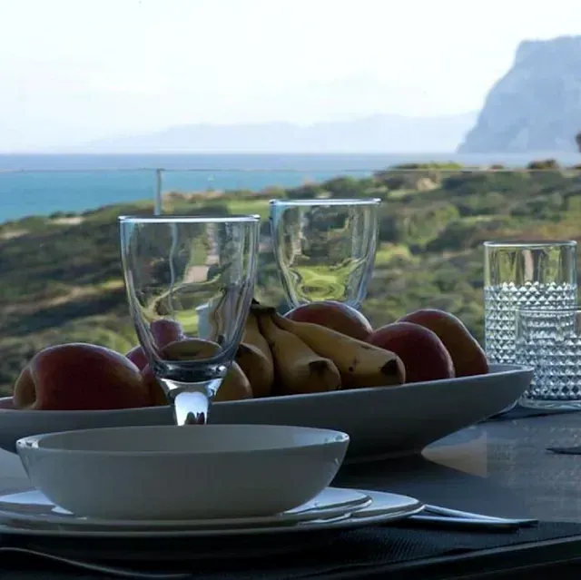 Mesa con frutero y vasos con vistas a un paisaje costero.