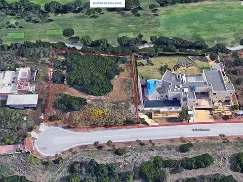 Vista aérea de un terreno delimitado en rojo, junto a una casa de lujo con piscina y campo de golf.