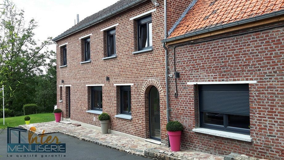 Façade d'une maison en briques. menuiseries pvc en gris anthracite RAL 7016 avec volets roulants incorporés. Porte fenetre plein cintre.