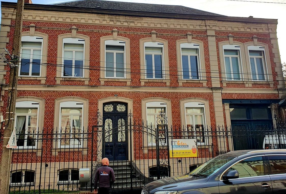 Façade d'une grande maison avec un portail en métal noir. fenetres en pvc blanc avec volets roulants motorisés solaires.
