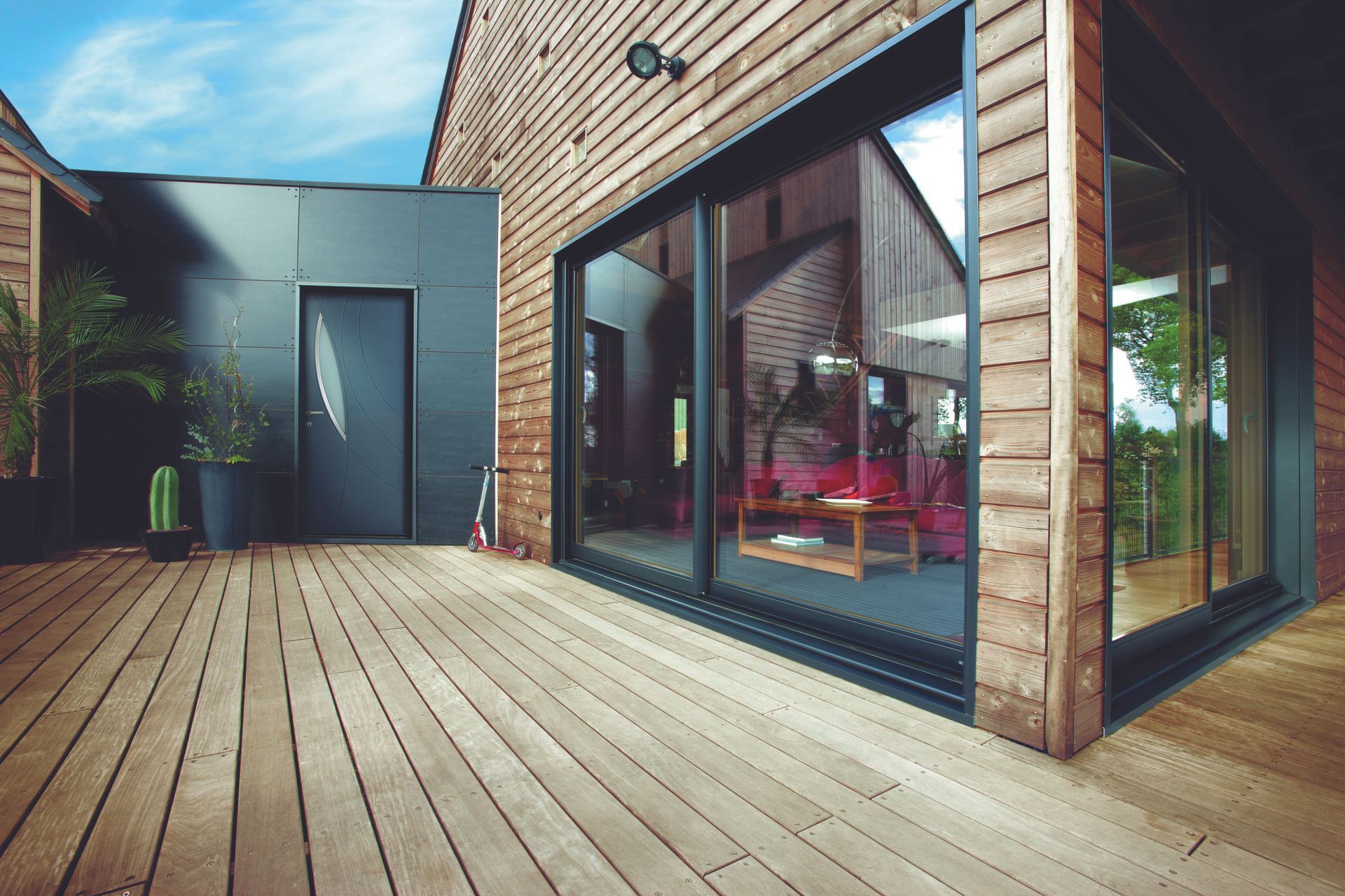 Porte-fenêtre coulissante en aluminium. terrasse bois. bardage bois. porte d'entrée en aluminium.