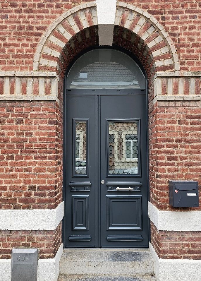 Double porte d'entrée en aluminium RAL 7016 gris anthracite surmontée d'une imposte fixe vitrée en forme plein cintre. Porte d'entrée avec grille. EURADIF.