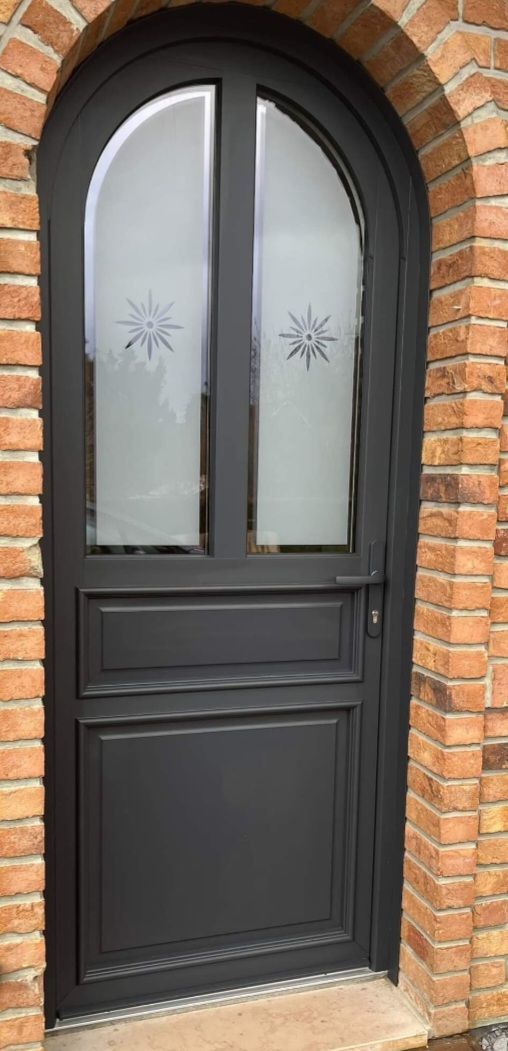 Porte d'entrée plein cintre en PVC noir RAL approchant 9005. Meneau central et vitrage décoratif. Fabricant PIERRET.