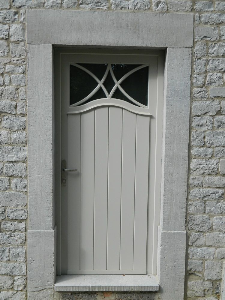 Porte d’entrée en bois gris avec partie vitrée avec entrelacements sur le haut.  Fabricant PIERRET.