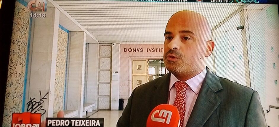Um homem de terno e gravata está falando em um microfone com pedro teixeira escrito na tela atrás dele