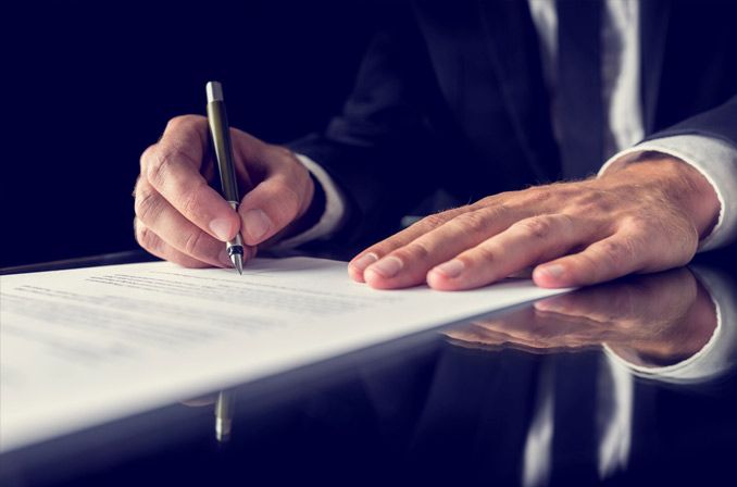 Un hombre con traje está escribiendo en un trozo de papel con un bolígrafo.