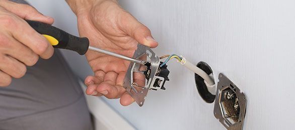 Un hombre está arreglando un tomacorriente eléctrico con un destornillador.
