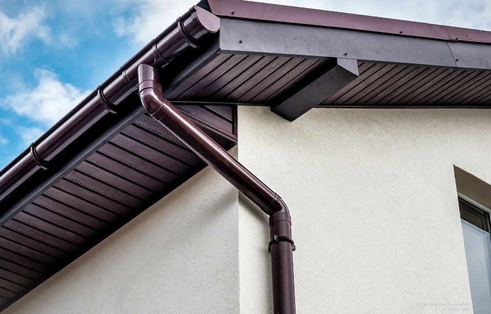 Graue Metalldachziegel auf einem Haus mit einem gemauerten Schornstein.