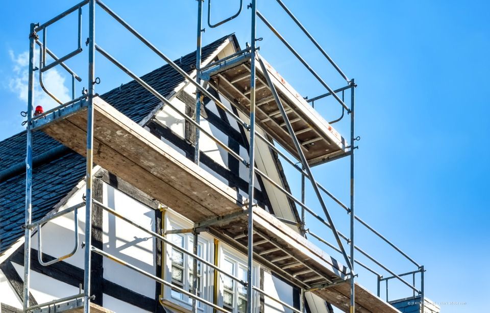 Braune Regenrinne und Fallrohr an einem cremefarbenen Haus mit dunkelbrauner Dachuntersicht. Blauer Himmel sichtbar.