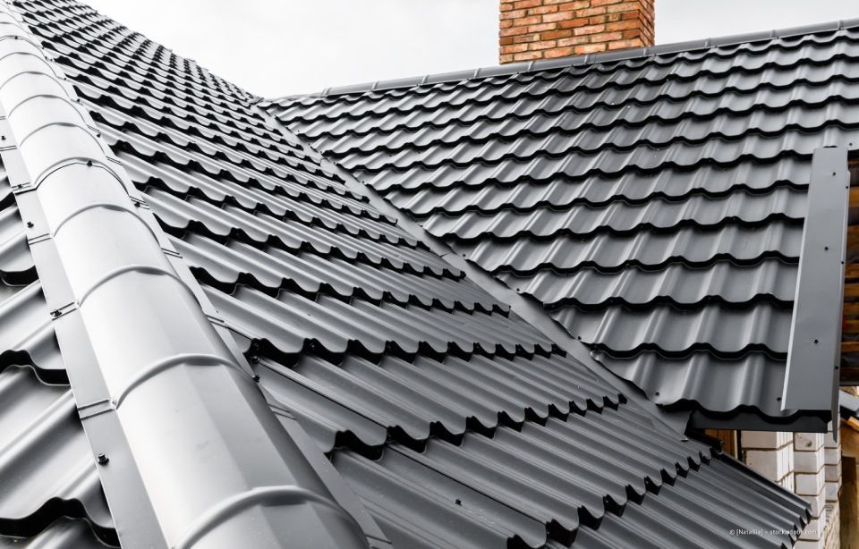 Dachdecker arbeiten unter einem teilweise bewölkten Himmel auf einem Dach und bringen dunkelgraue Schindeln an.