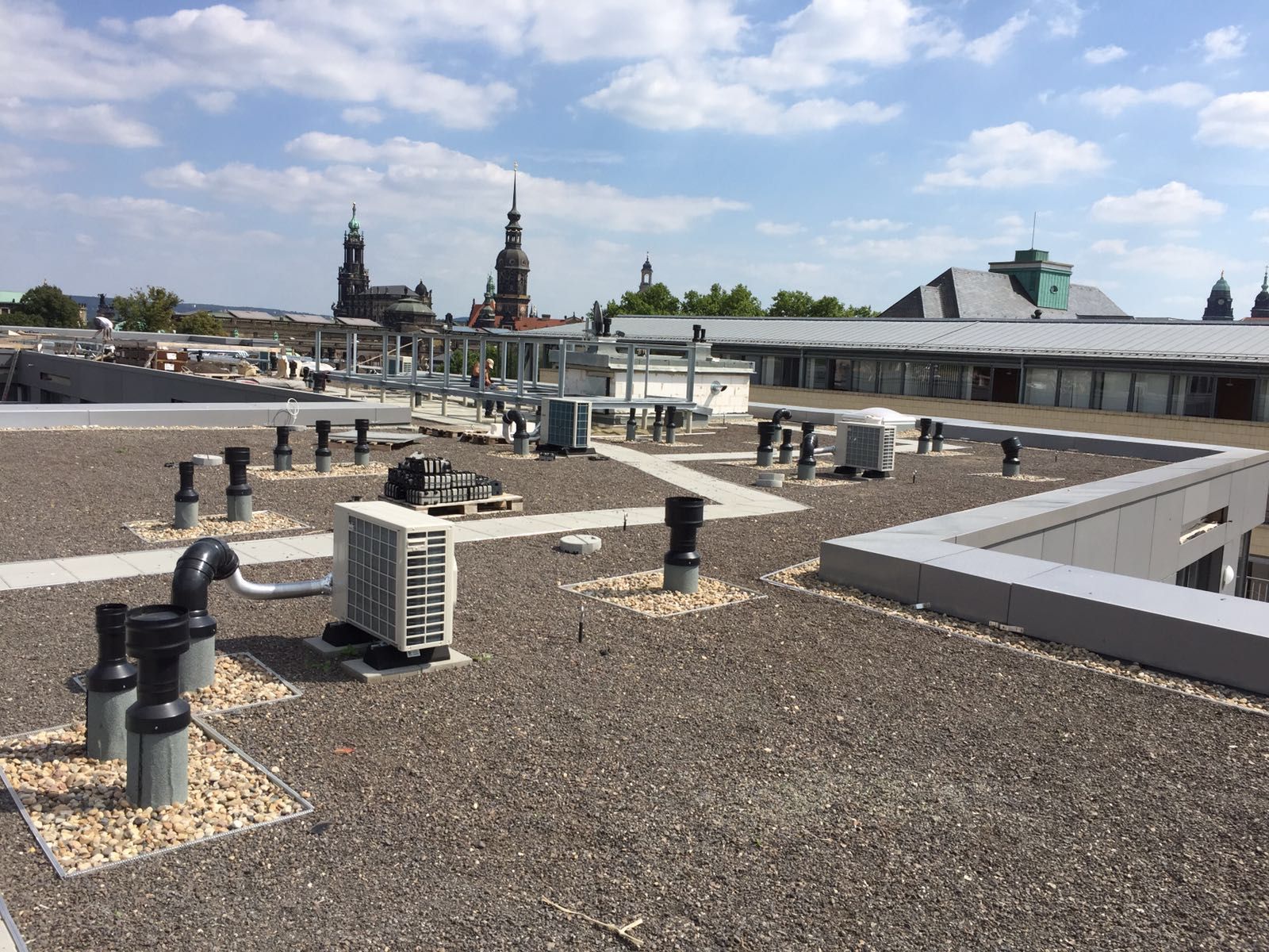 Person mit orangefarbenem Schutzhelm streicht eine Oberfläche mit einer Rolle schwarz, Eimer in der Nähe.