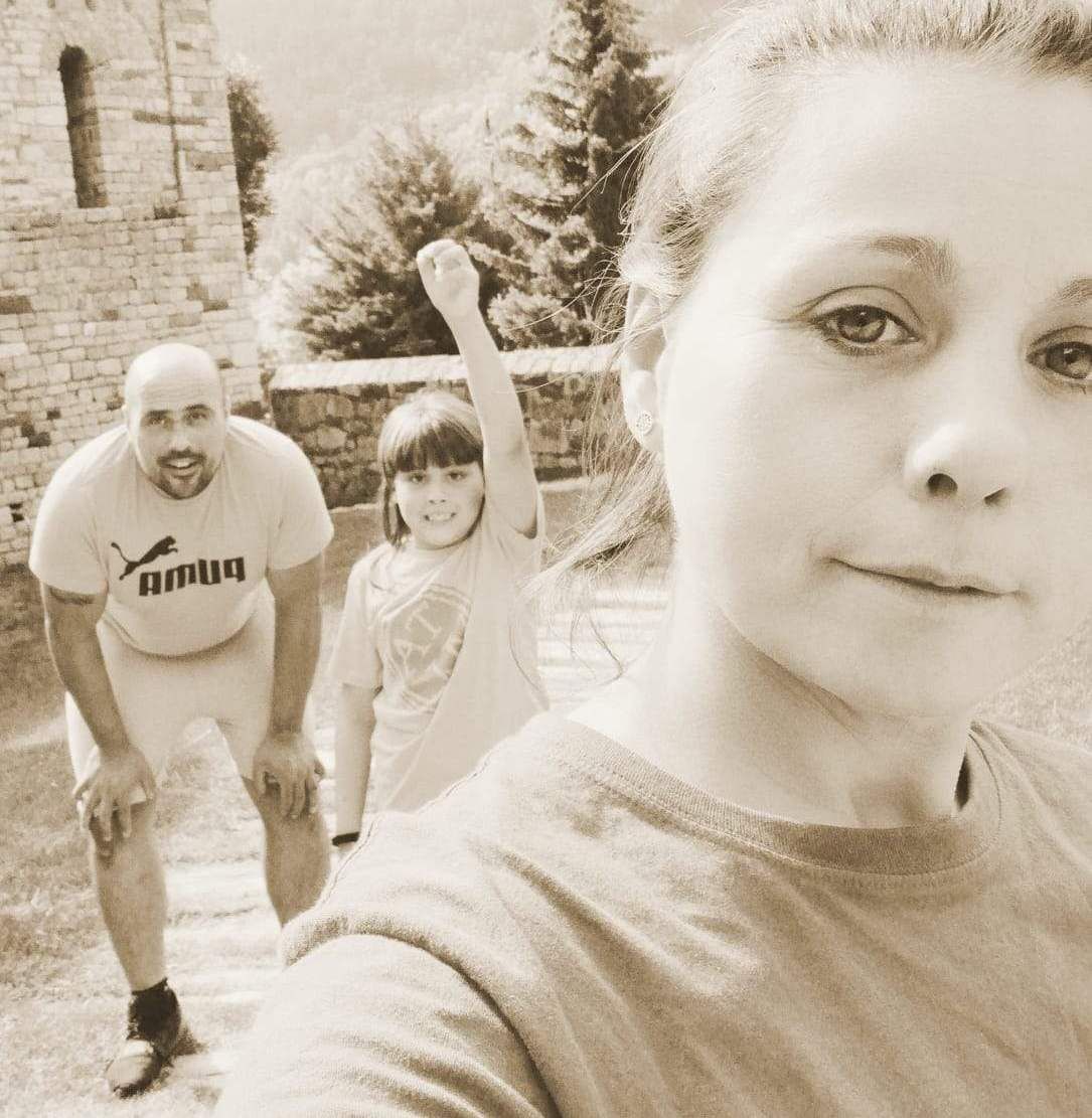 Dona fent-se un selfie amb un home i un nen a fora. El nen aixeca el braç, l'home s'ajup, edifici de pedra al fons. To sèpia.