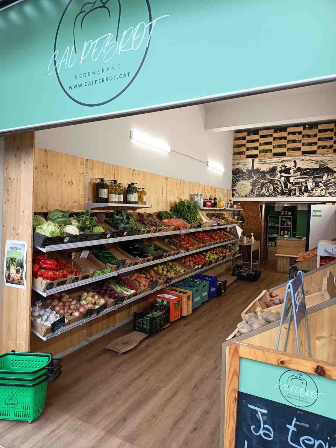 Interior d'una botiga de productes frescos amb prestatges que mostren diverses verdures i un rètol que diu