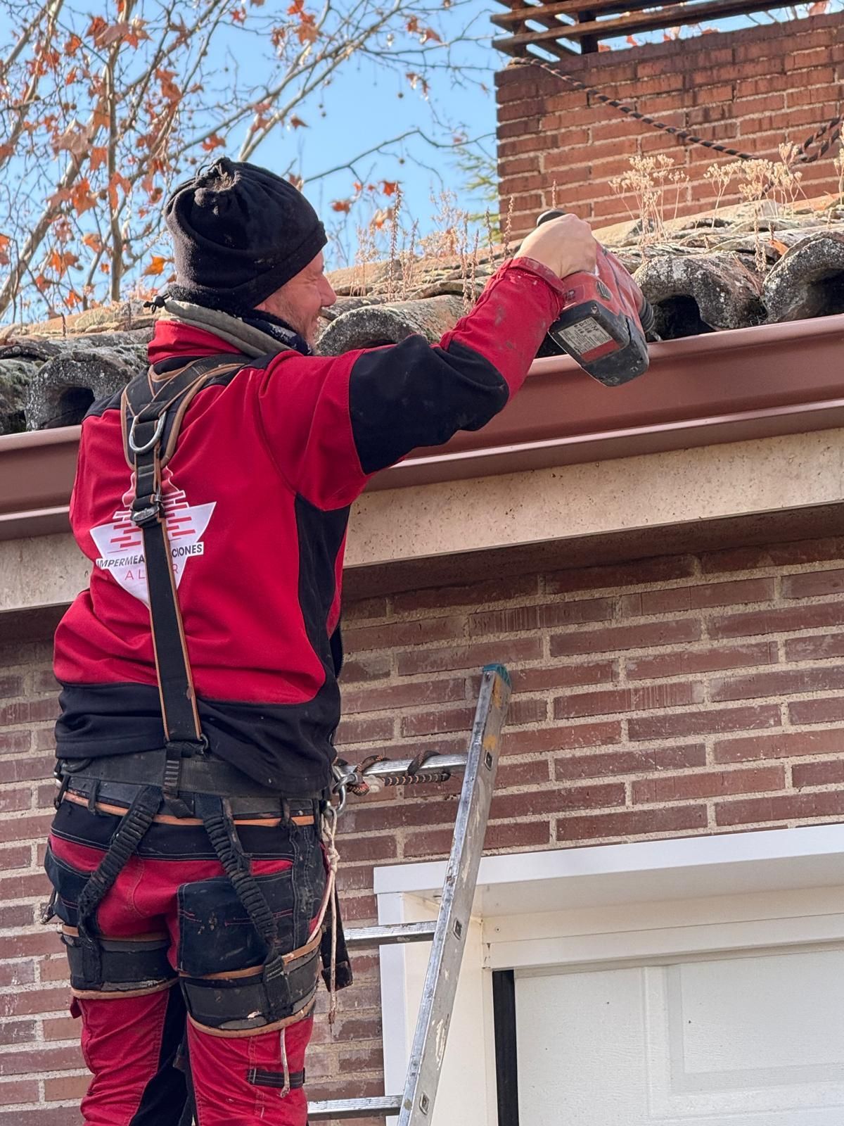 Un hombre está de pie en una escalera arreglando una canaleta en un edificio de ladrillos.