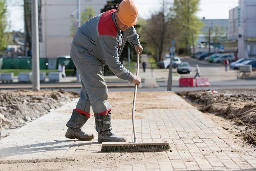 Un trabajador de la construcción está barriendo una acera con una escoba.