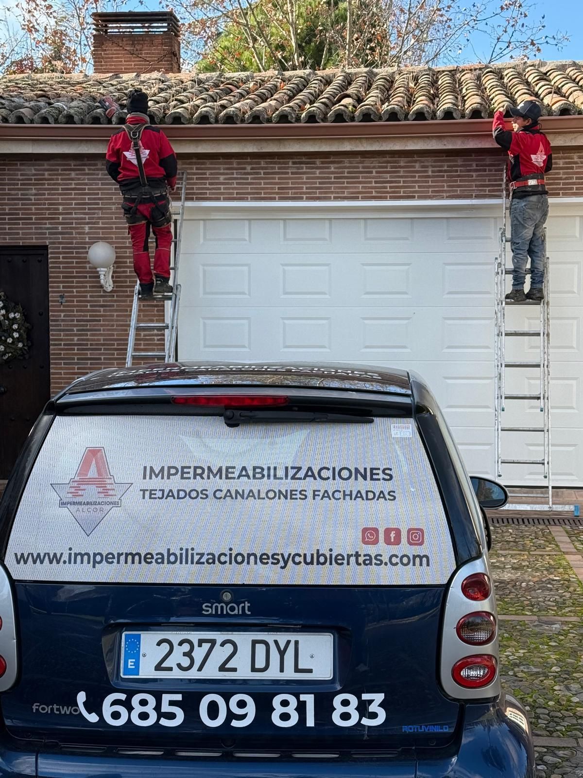 Dos hombres están trabajando en el tejado de una casa al lado de un coche.