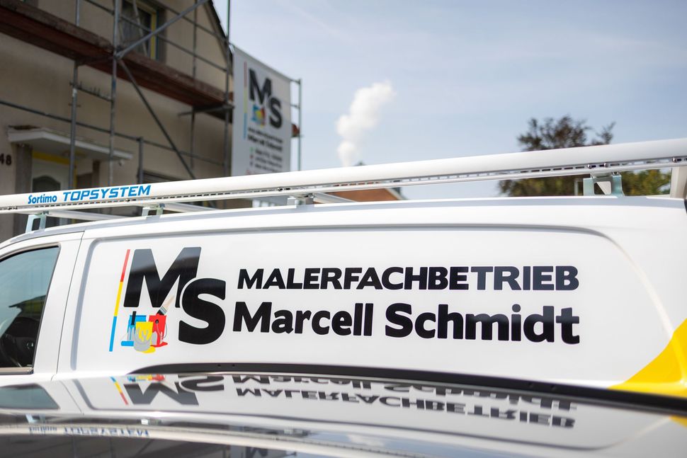 Weißer Lieferwagen mit dem Logo und dem Schriftzug „Malerfachbetrieb Marcell Schmidt“ an der Seite im Außenbereich