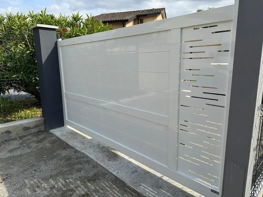 Portail coulissant gris moderne avec panneau décoratif ajouré, jouxtant un mur et une allée en béton.