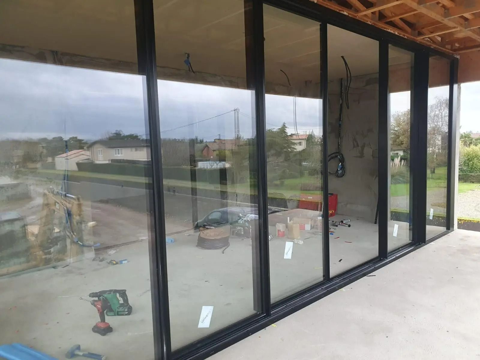 Chantier de construction avec de grandes baies vitrées réfléchissantes et des outils à l'intérieur d'un bâtiment moderne à l'extérieur