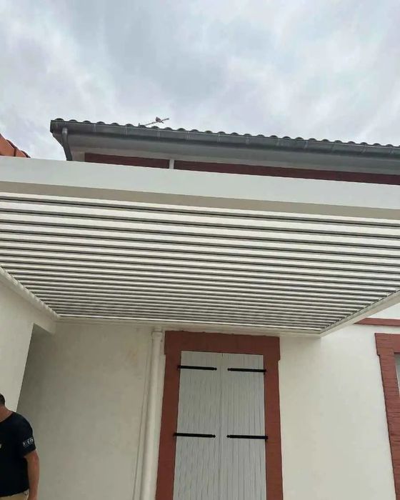 Entrée d'une maison avec un auvent en treillis blanc et des portes à encadrement rouge sous un ciel nuageux