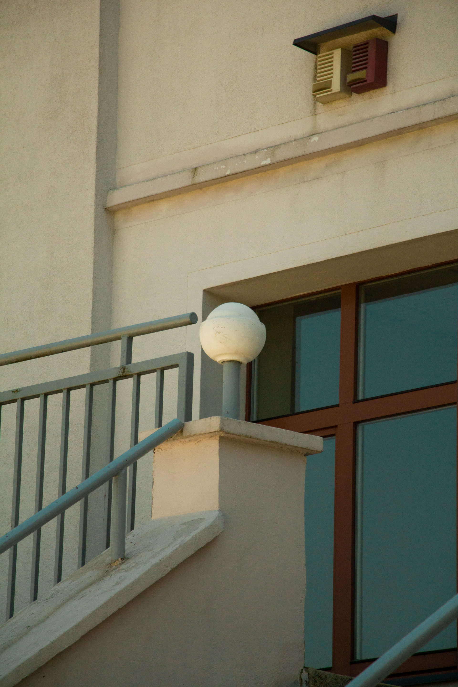 Escalier à côté d'un bâtiment beige avec une rampe blanche et une lampe ronde près d'une fenêtre