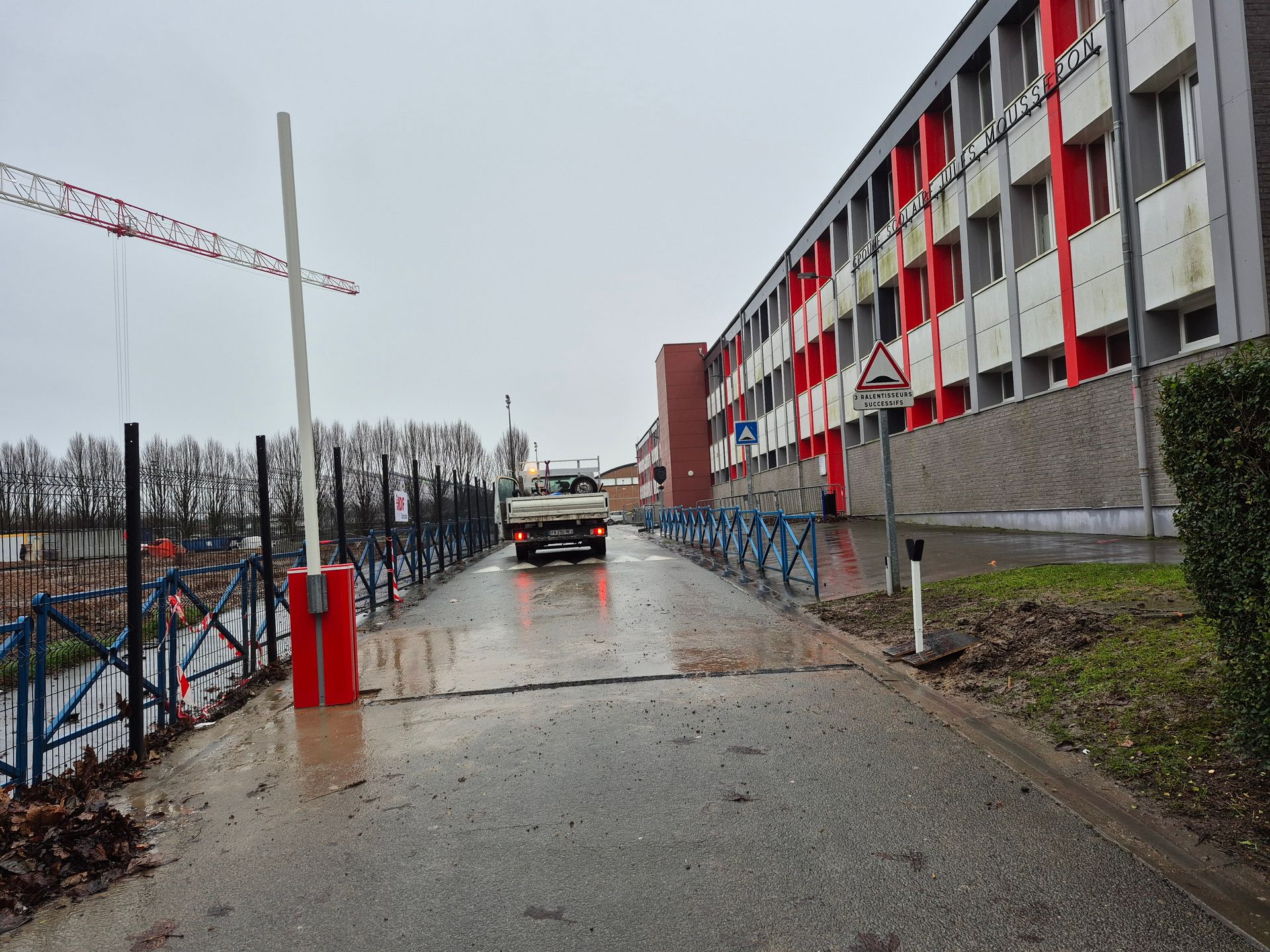 Une route mouillée avec une barrière, un camion et un bâtiment avec des colonnes rouges par temps nuageux.