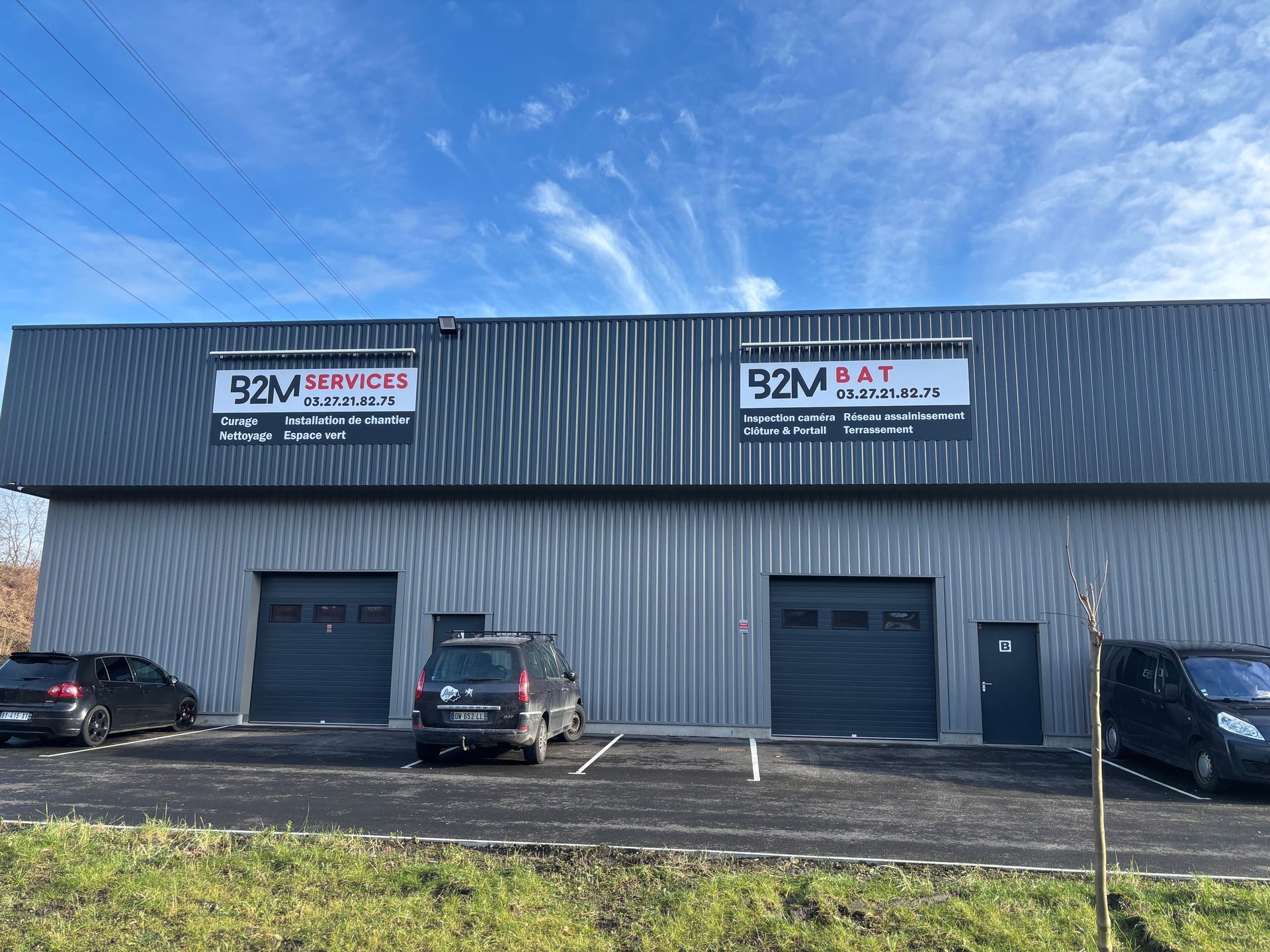Un bâtiment commercial avec trois portes de garage et des enseignes d'entreprise. Des voitures sont garées devant.