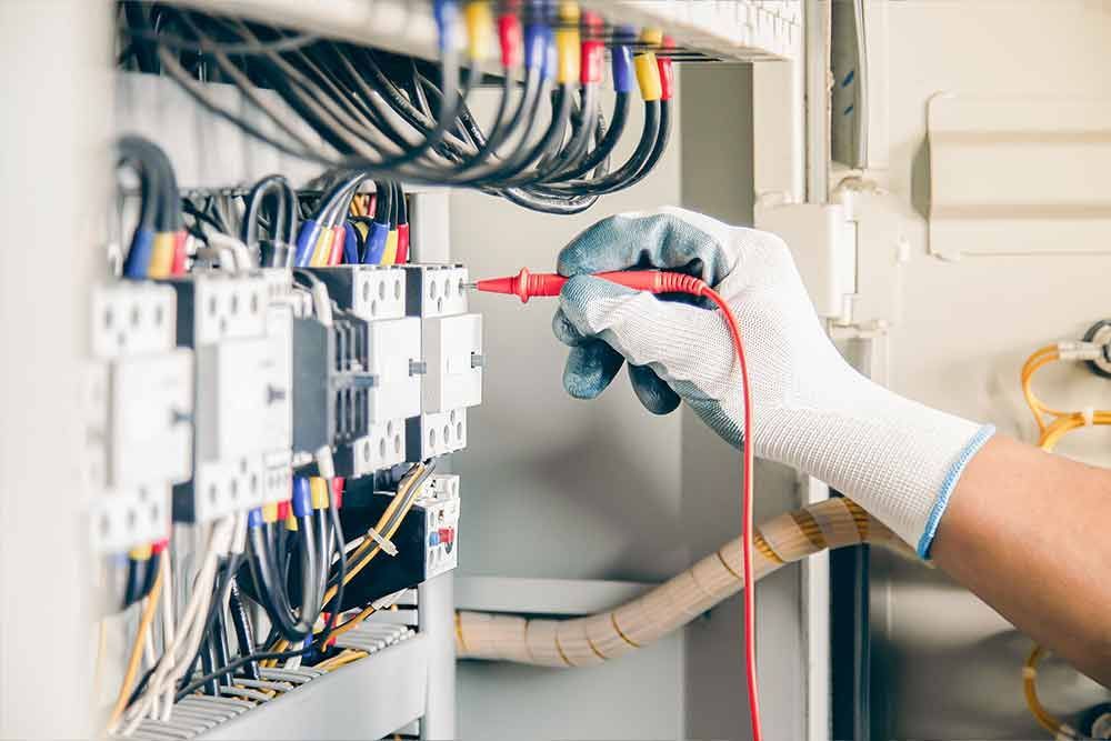 Ein Elektriker prüft die Verkabelung in einem Verteilerkasten mit einem Multimeter.