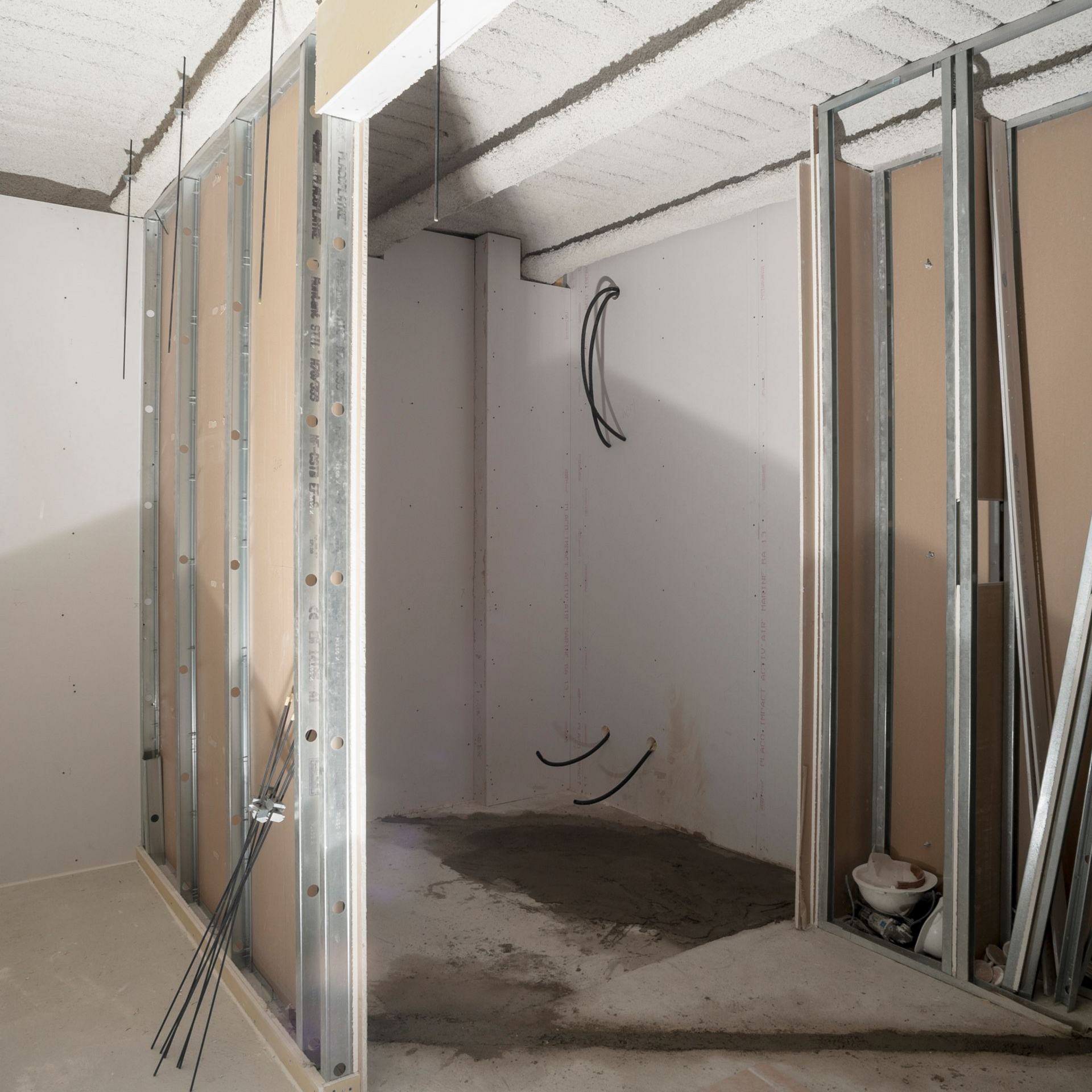 Intérieur d'une pièce en construction, avec des montants métalliques et des plaques de plâtre partiellement installés.