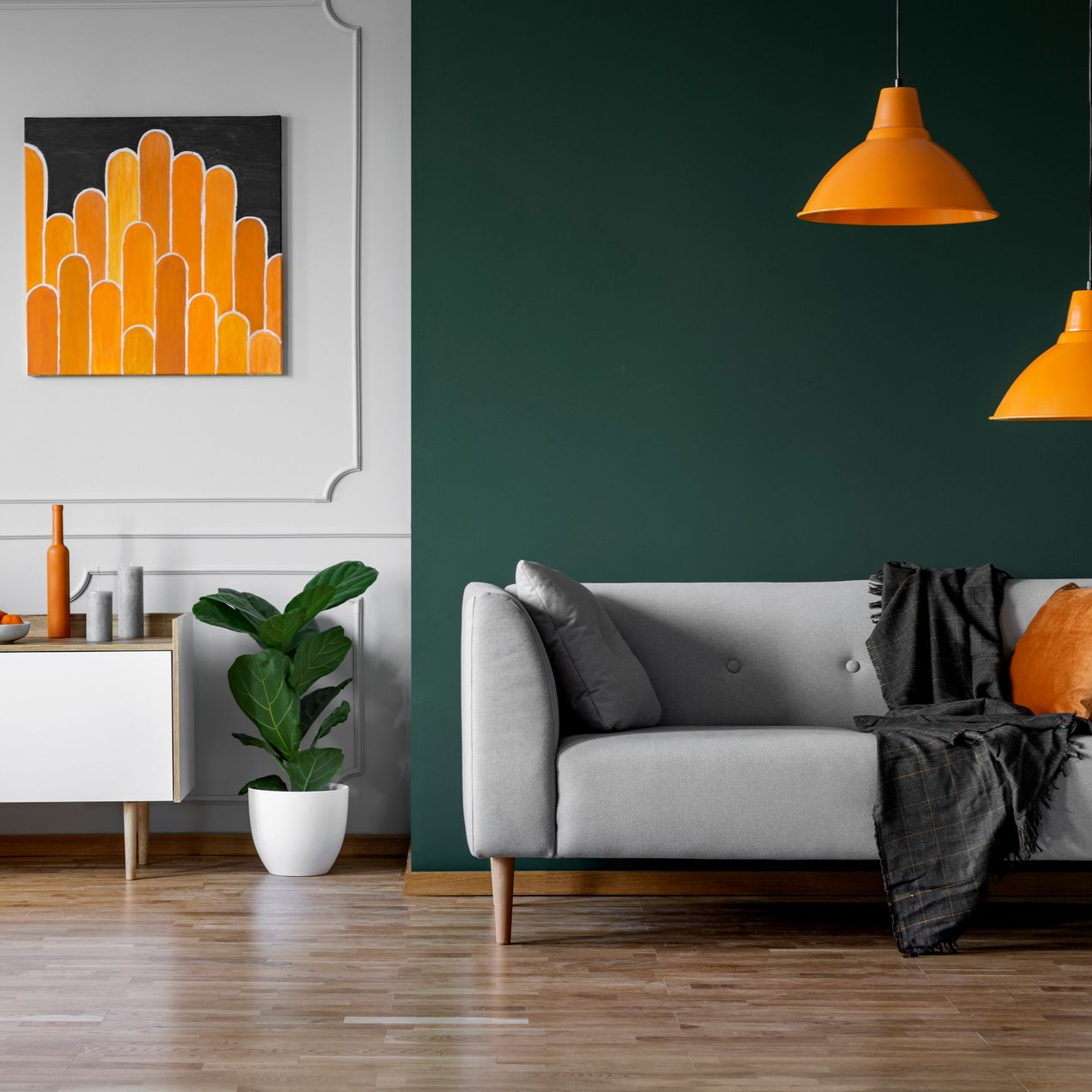 Salon avec canapé gris, lampes orange, mur vert et œuvres d'art.