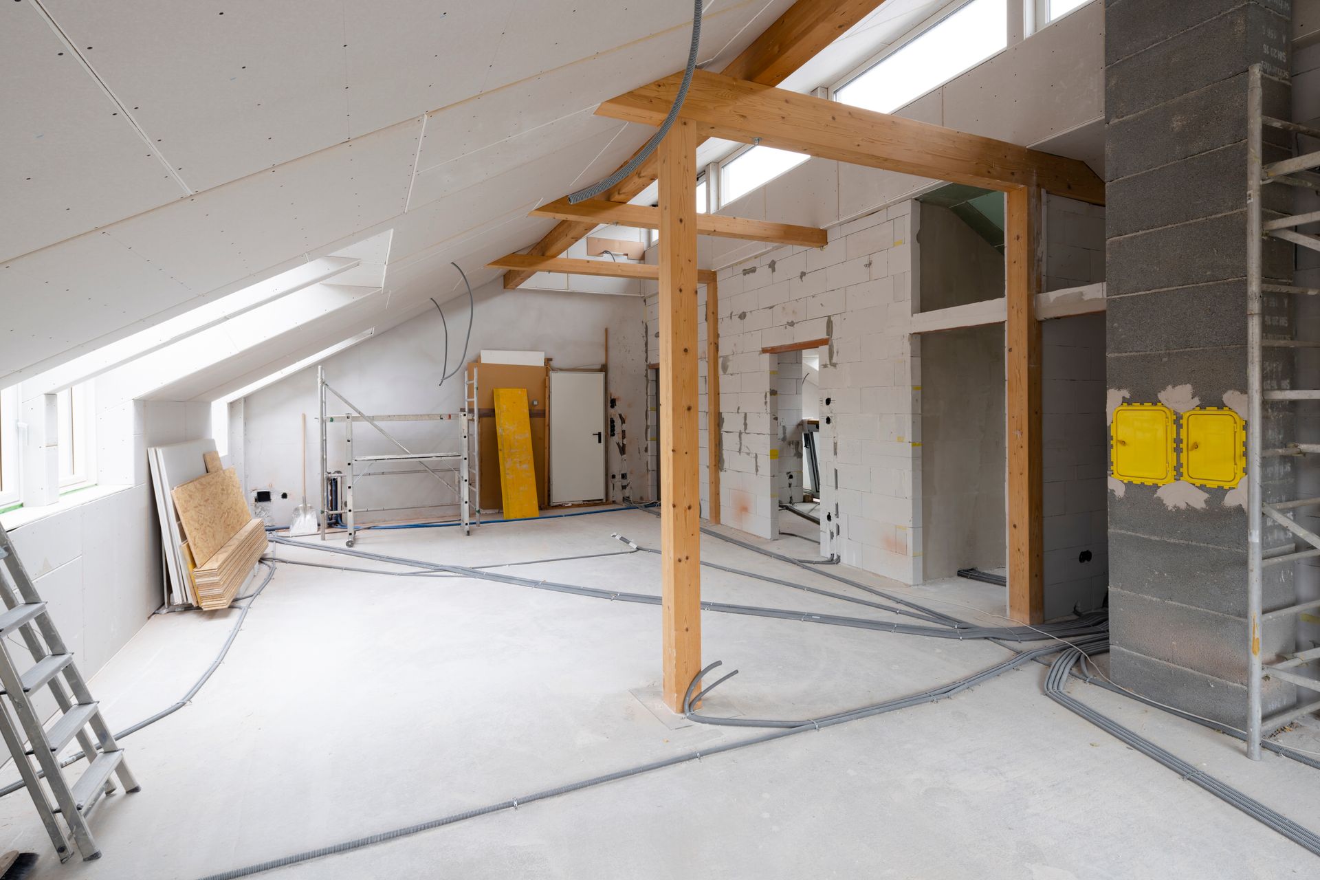 Chantier de construction intérieur avec poutres en bois apparentes, câblage et murs inachevés.