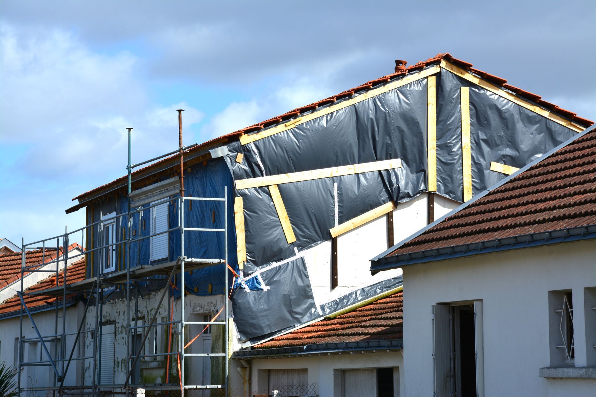 Surélévation en construction, murs apparents recouverts d'une bâche noire, échafaudages et toit de tuiles rouges.