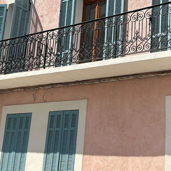 Immeuble en stuc rose avec volets bleus et balustrade de balcon noire ornée.