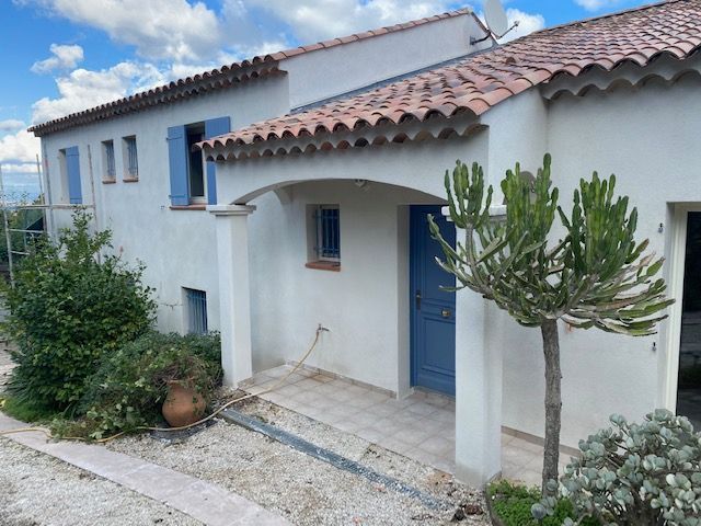 Maison en stuc blanc avec toit en tuiles de terre cuite, volets et porte bleus, petit porche.