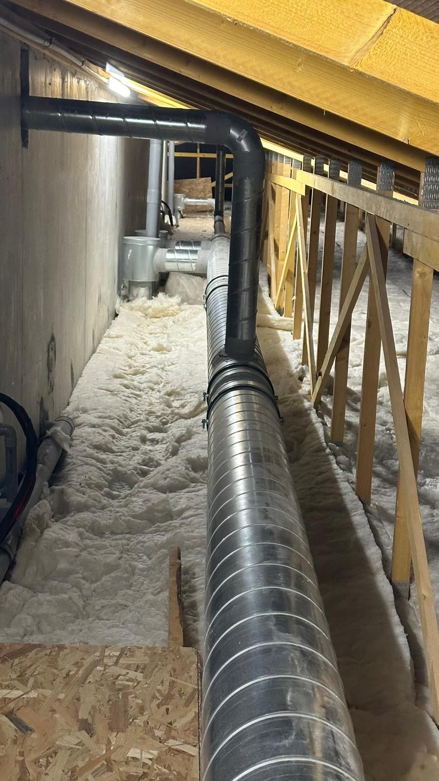 Un grenier avec des conduits de ventilation et d'isolation. Les conduits sont argentés et noirs et recouverts d'isolant.