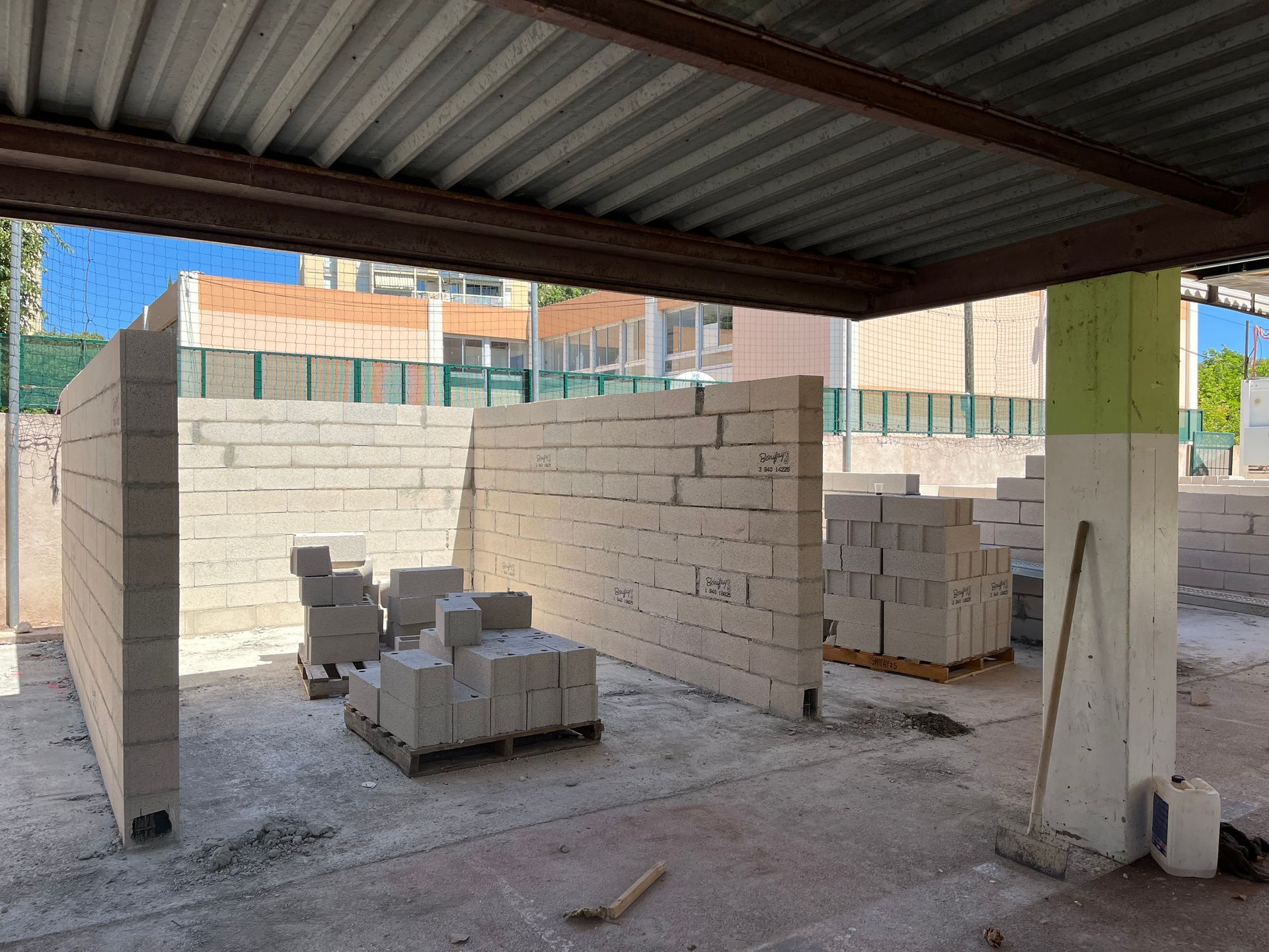 Chantier sous un auvent métallique. Murs construits en parpaings clairs. Le matériel et les outils sont visibles.
