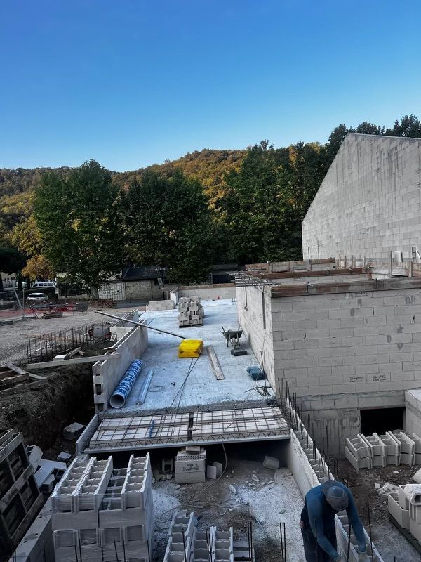Chantier de construction avec murs en parpaings, dalle de béton et un ouvrier.