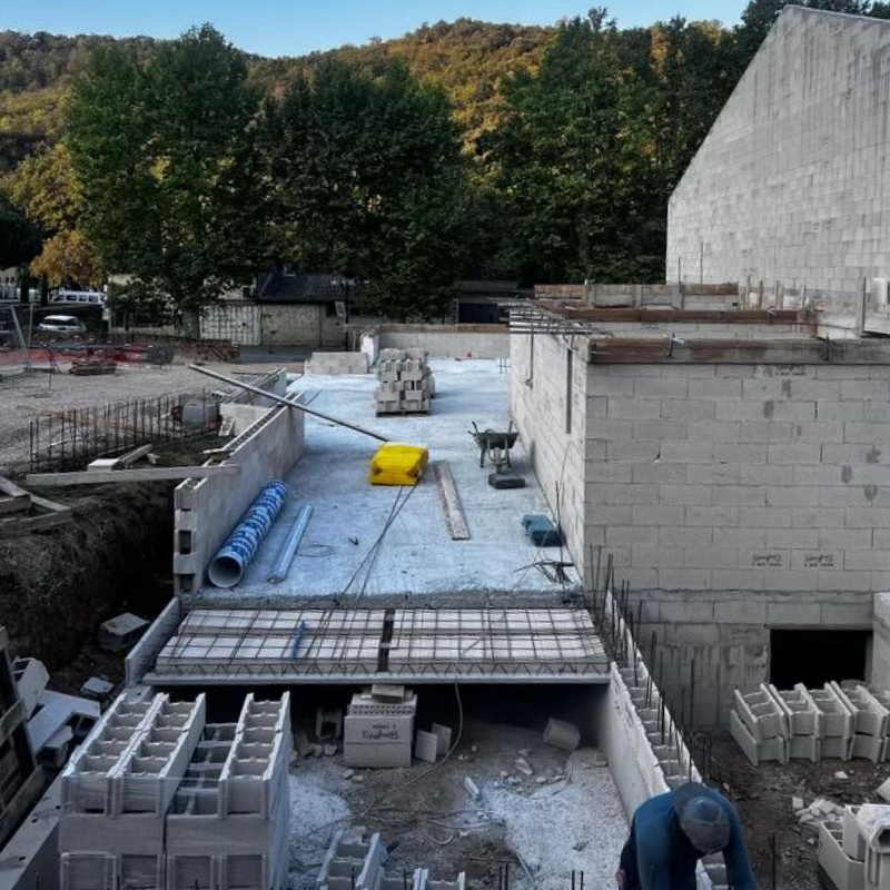 Chantier de construction avec murs en parpaings, dalle de béton et un ouvrier.
