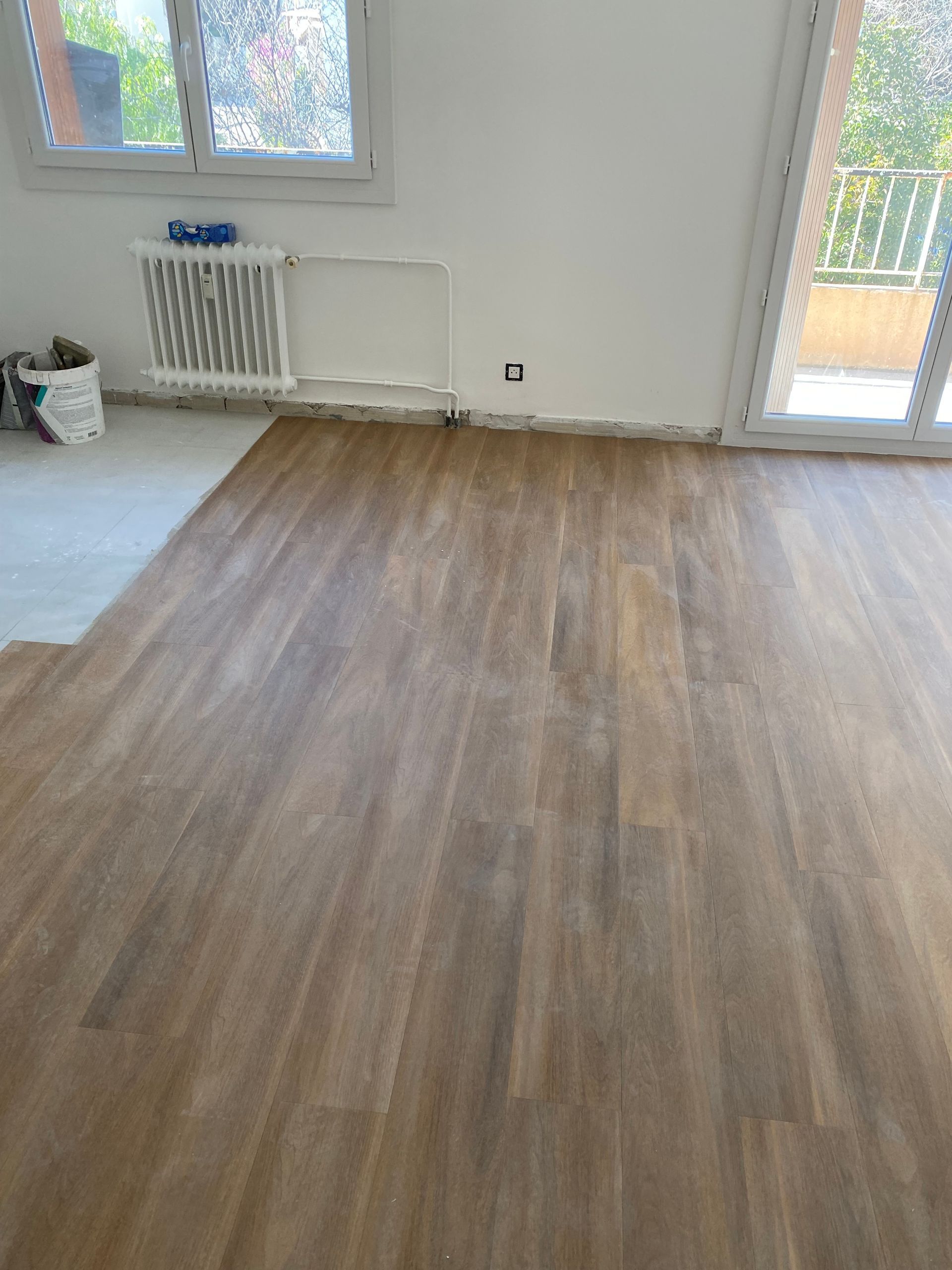 Pose de parquet dans une pièce avec fenêtre et porte donnant sur un balcon.