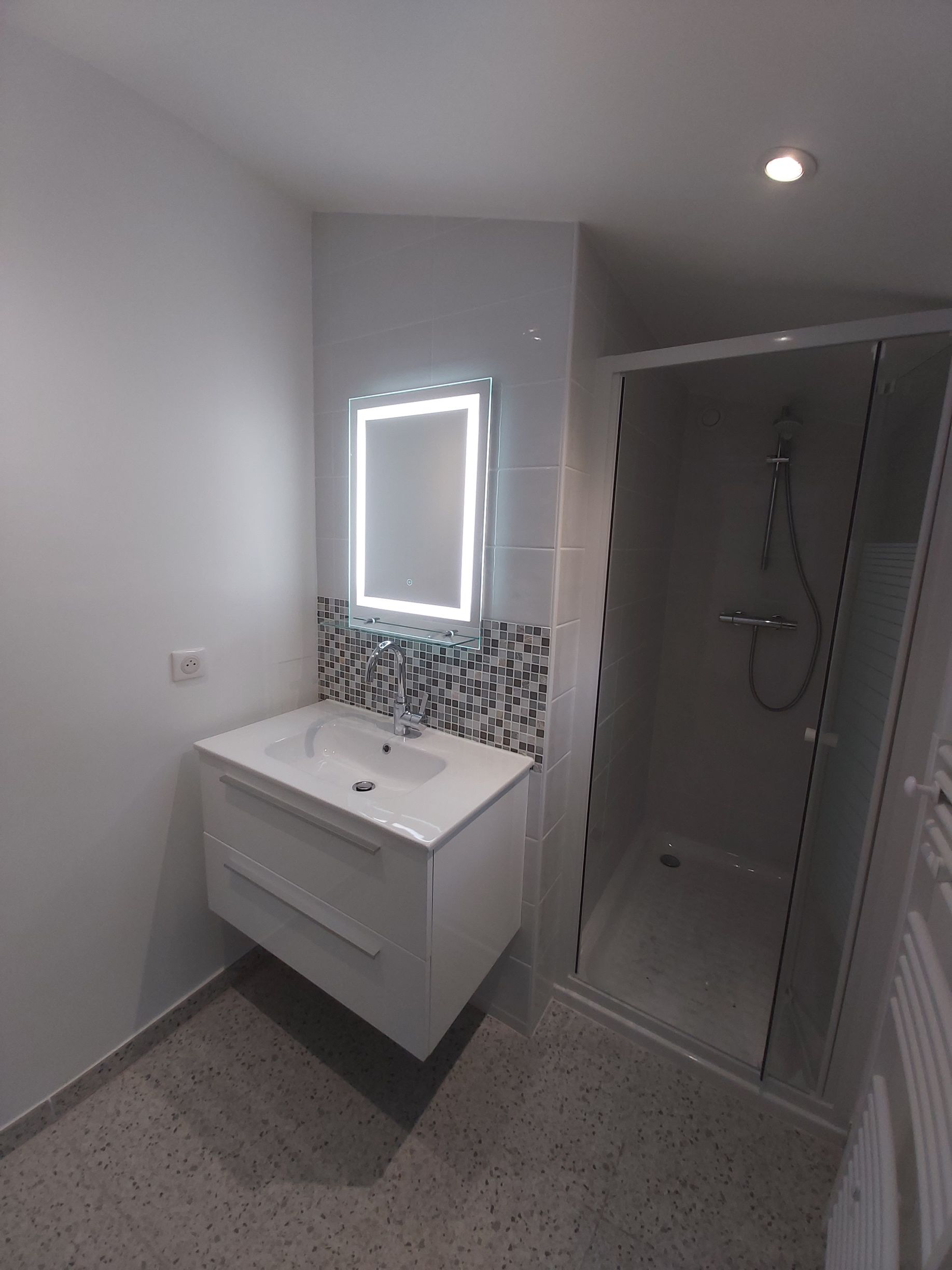 Salle de bains moderne blanche avec lavabo, miroir et douche vitrée.