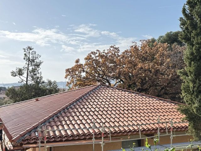 Toit de tuiles en terre cuite, arbres et ciel bleu.