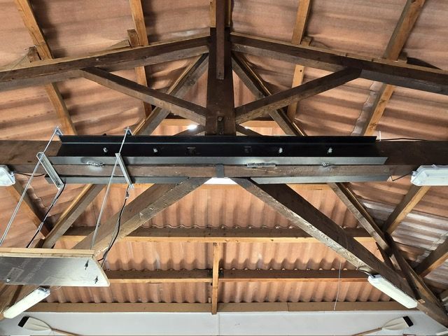 Chevrons et poutres en bois soutenant un toit. Un objet noir et rectangulaire est suspendu à une poutre.
