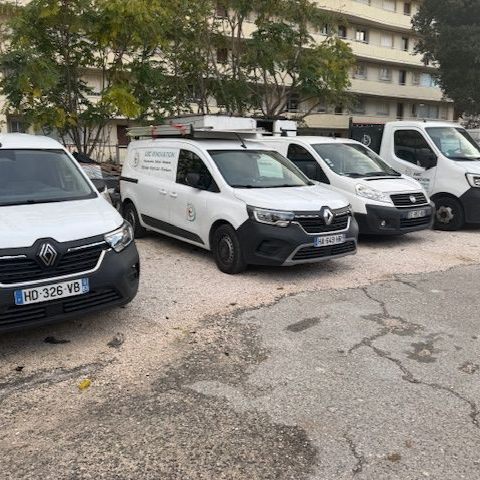 Cinq fourgonnettes commerciales blanches étaient garées à l'extérieur, devant un bâtiment.