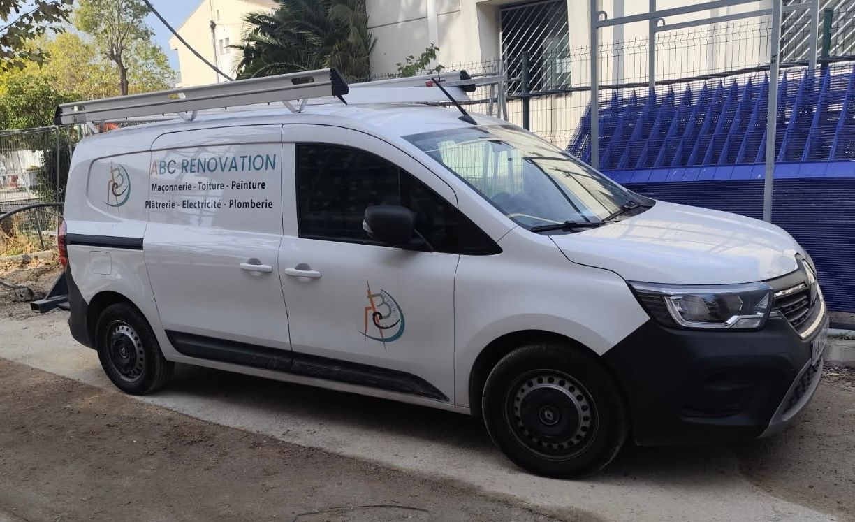 Fourgonnette de service blanche avec logo « PRESERVATION », stationnée dans la rue. Échelle sur le toit, clôture de chantier bleue en arrière-plan.