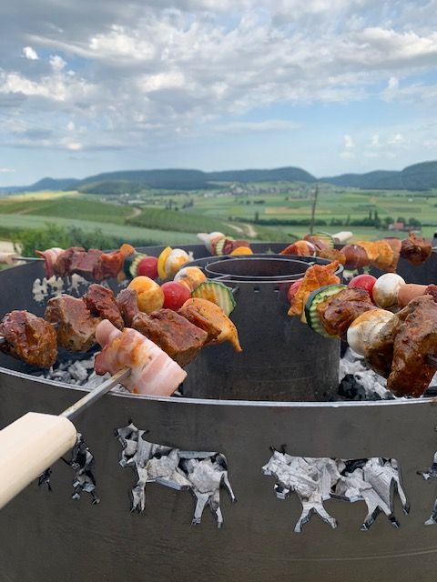 Rippchen und anderes Fleisch werden auf einer grossen, flachen, runden Feuerstelle gegrillt. Flammen schlagen hoch.