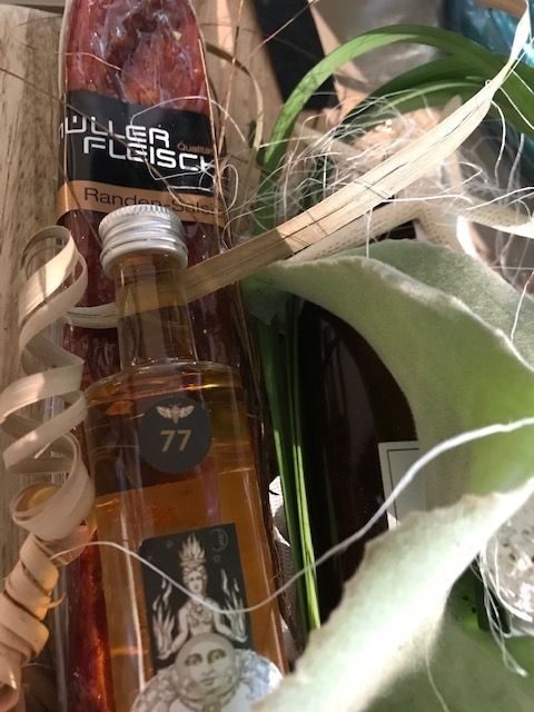 Nahaufnahme eines Geschenkkorbs mit einer Wurst, einer Schnapsflasche, Grünzeug und dekorativen Elementen.