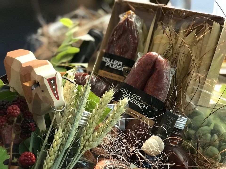 Geschenkkorb mit Würstchen, Holzkuh, Grünzeug und kleinen Flaschen.