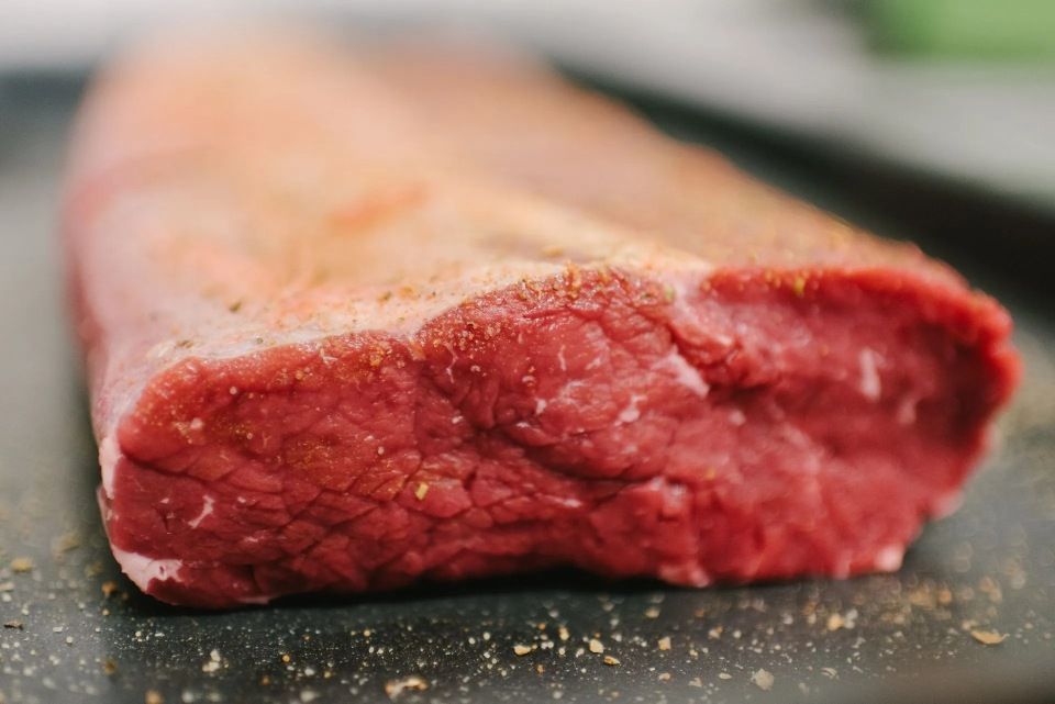 Nahaufnahme von rohem, rotem Rinderfilet auf dunklem Untergrund, gewürzt mit Gewürzen.