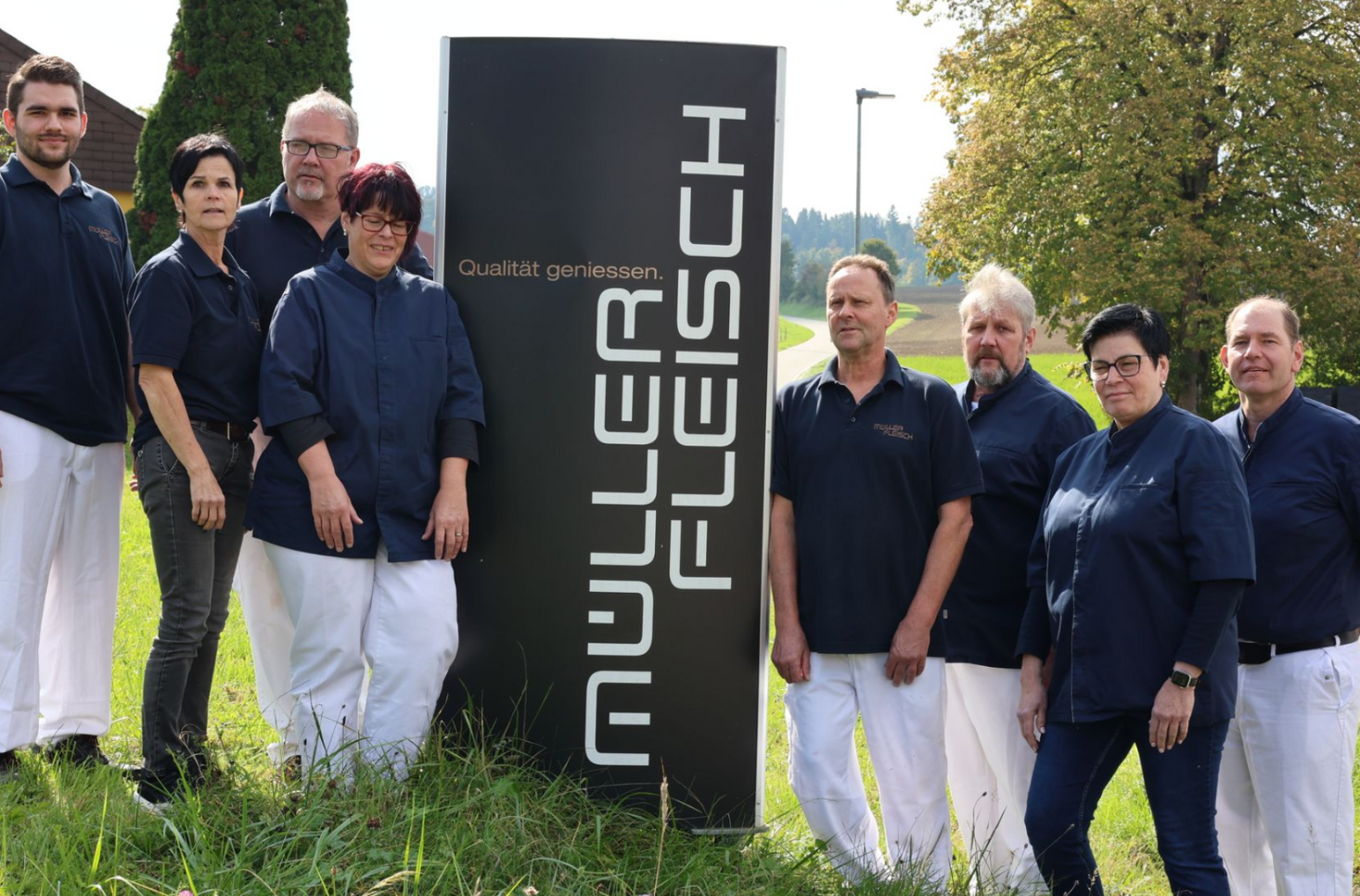 Zwei Männer grillen Essen auf Grillplatten vor einer Backsteinmauer. Einer benutzt einen Pfannenwender.