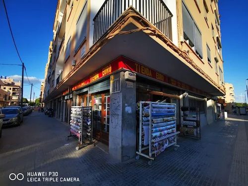 Esquina de un edificio con escaparates, toldos y expositores en la acera en un día soleado.